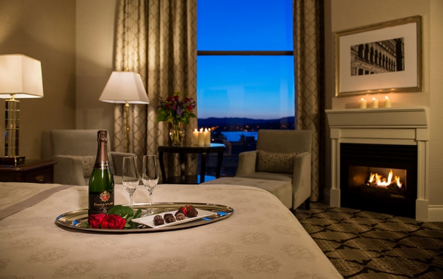 Champagne with 2 glasses on tray with chocolate and chocolate covered strawberries with a fire in fireplace and evening view of inner harbour.