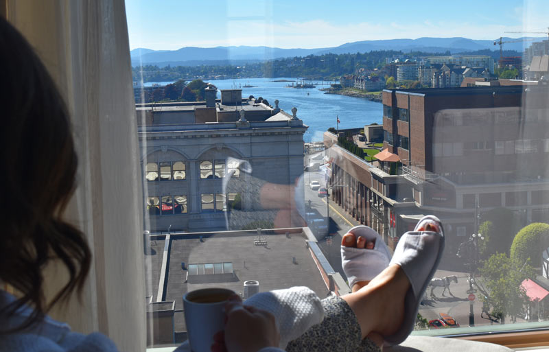 aha moment, women with slippers, feet, drinking coffee looking out grand window with view of water, buildings, and Scenic Bay Hotel life.