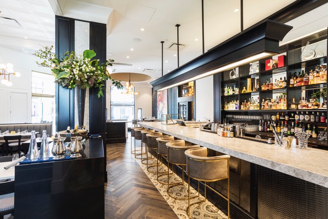 Two queen beds in brightly lit room with floor to ceiling windows. Ornate carpets and cozy bedding with a white orchid on table by window.